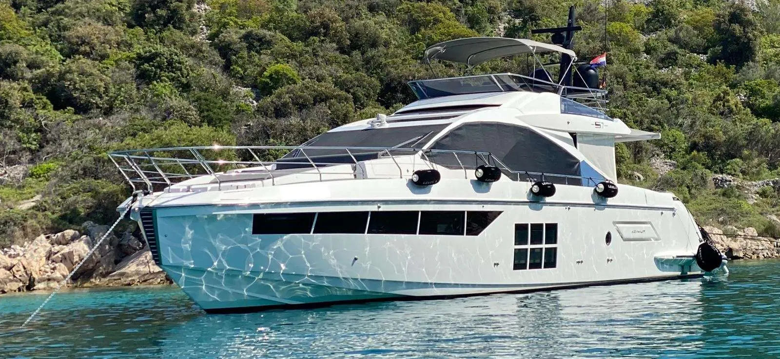 Azimut S7 — Bateau à moteur blanc vu de profil, amarré devant une côte rocheuse.