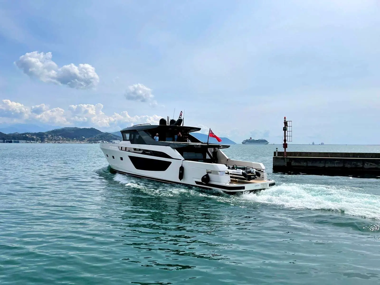 Bluegame BGX 70 — Bateau à moteur blanc vu de trois quarts arrière, naviguant près d'une jetée.