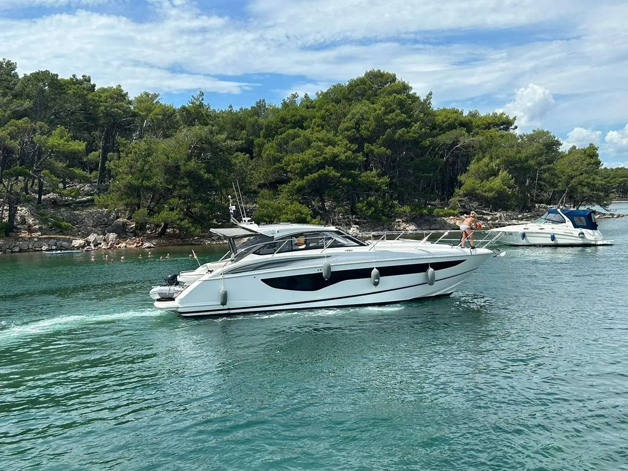 Princess V40 — Vedette blanche photographiée de profil sur une eau turquoise, près d'une côte boisée.