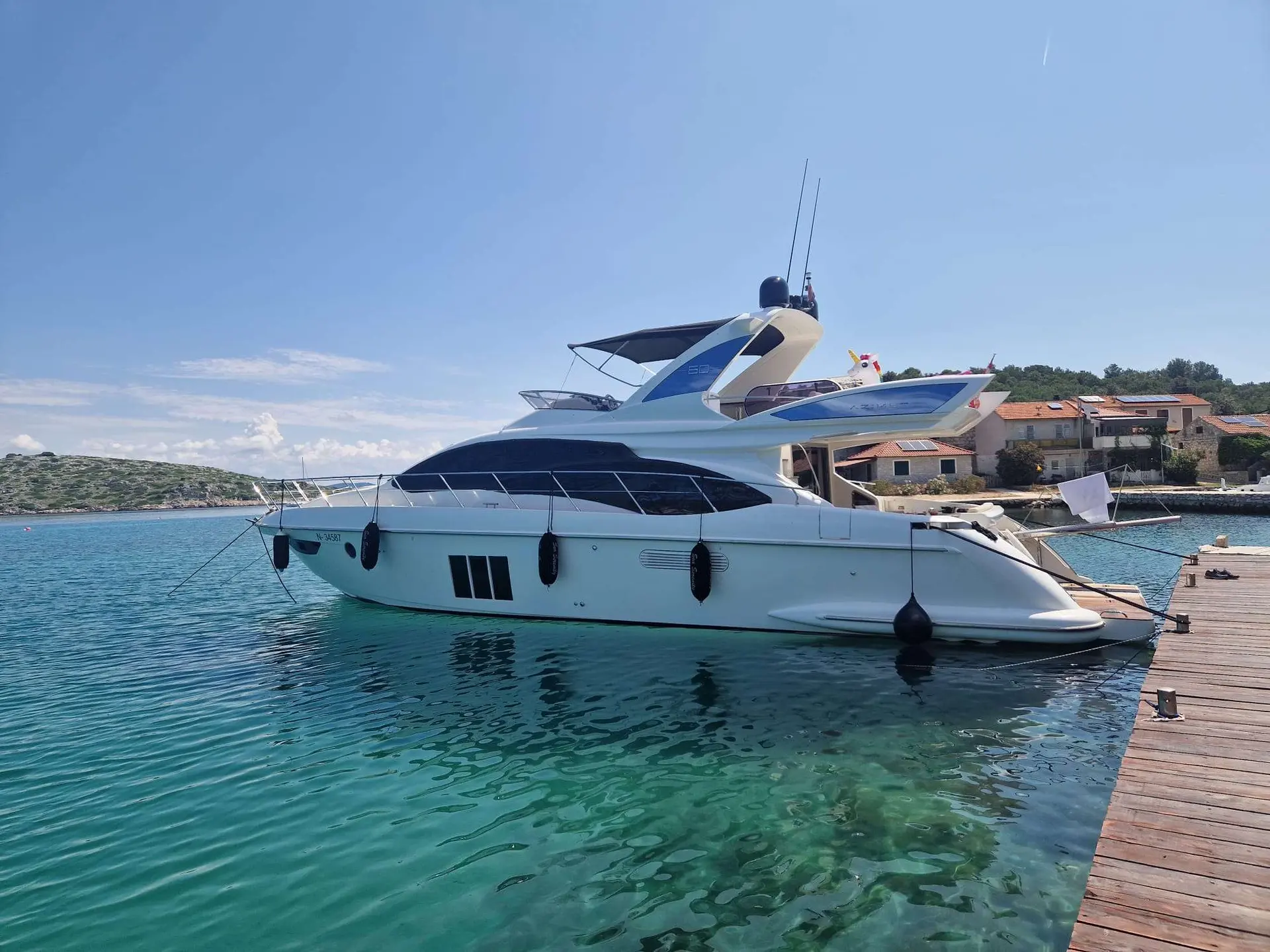 Azimut 60 Fly — Bateau à moteur blanc amarré le long d’un ponton, dans une baie ensoleillée.