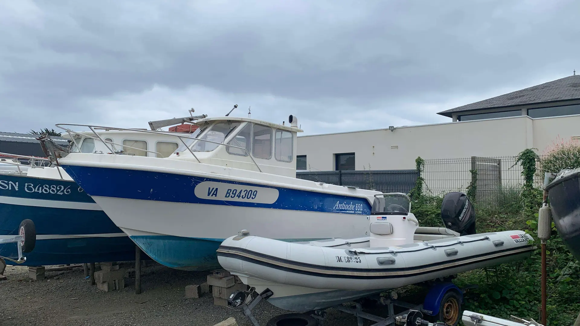 Guymarine Antioche 650 — Bateau à cabine bleu et blanc stationné à terre, partiellement masqué par un semi-rigide.