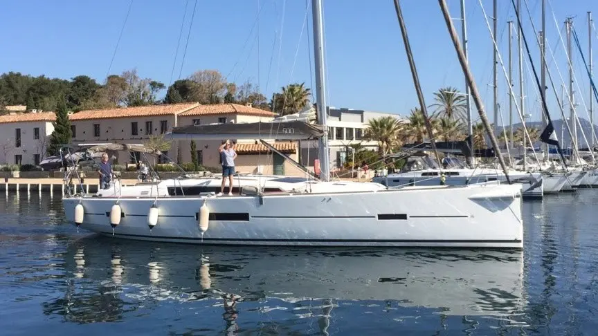 Dufour 500 Grand Large — Voilier blanc vu de profil dans un port, avec des personnes à bord.