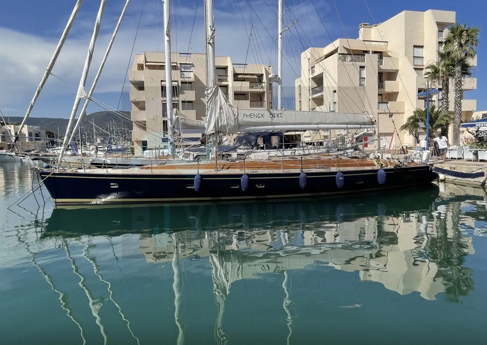 Custom Phenix Dixi — Voilier amarré de profil dans un port, avec ses voiles ferlées.