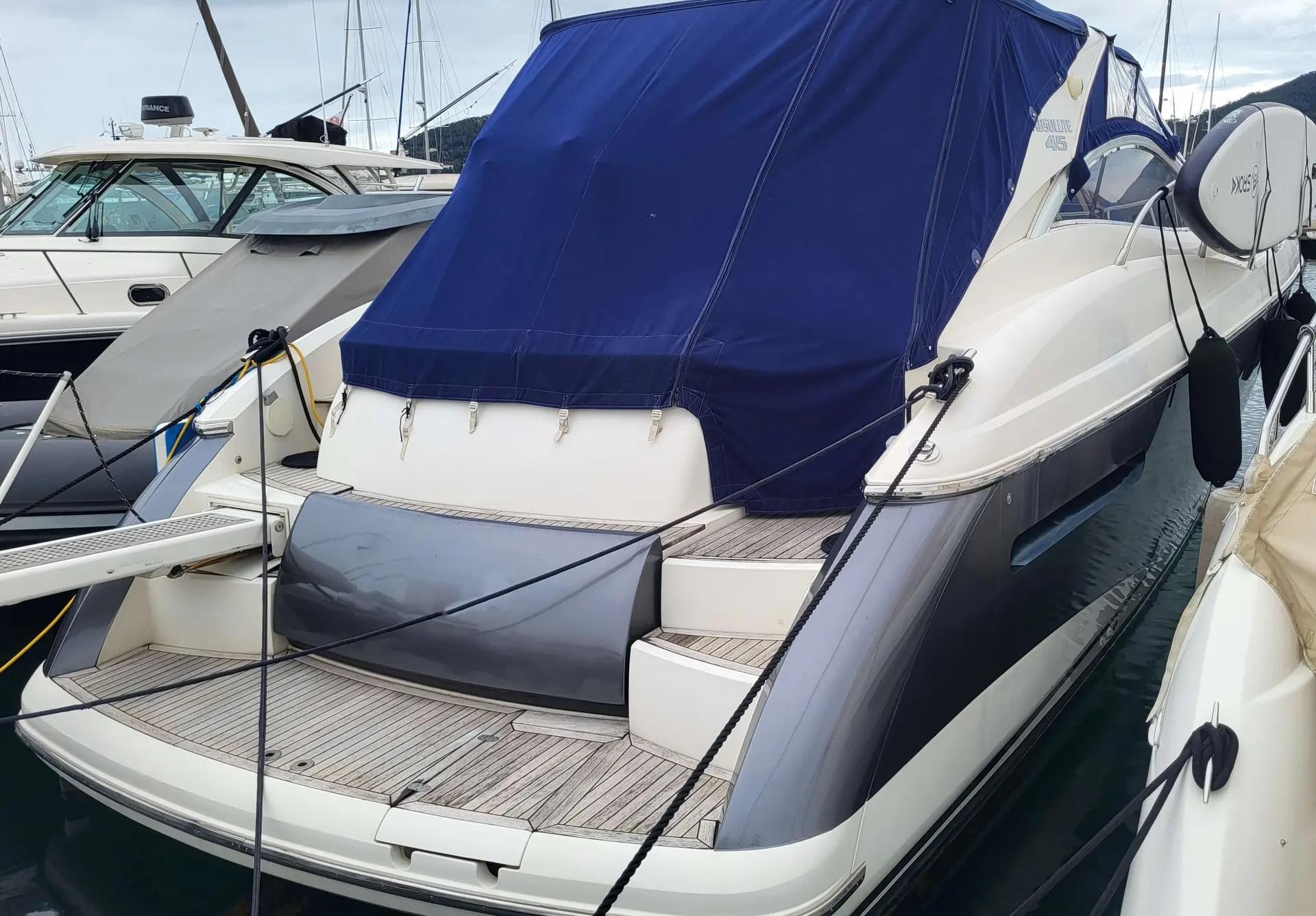 Absolute 45 — Vue arrière trois-quarts d’un bateau à moteur amarré, avec taud bleu fermé.