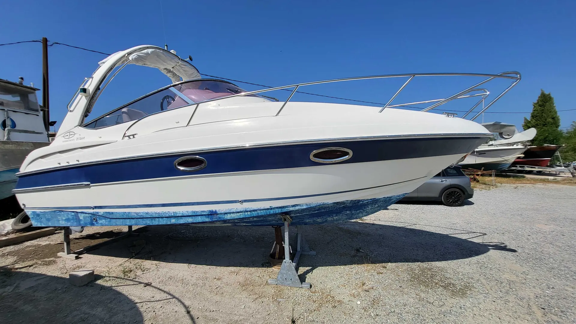 Bavaria 25 Sport — Bateau à moteur blanc et bleu présenté à terre, vu de profil dans une cour nautique.