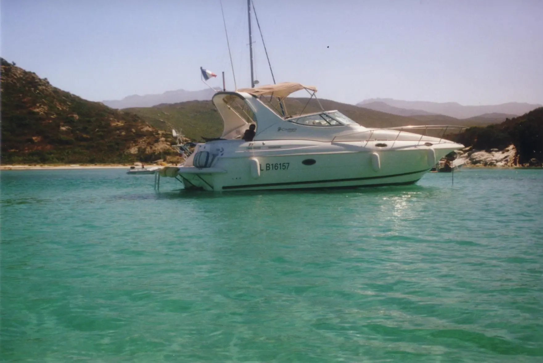 Cruisers Yachts 3075 Express — Bateau à moteur vu de profil dans une baie entourée de collines.