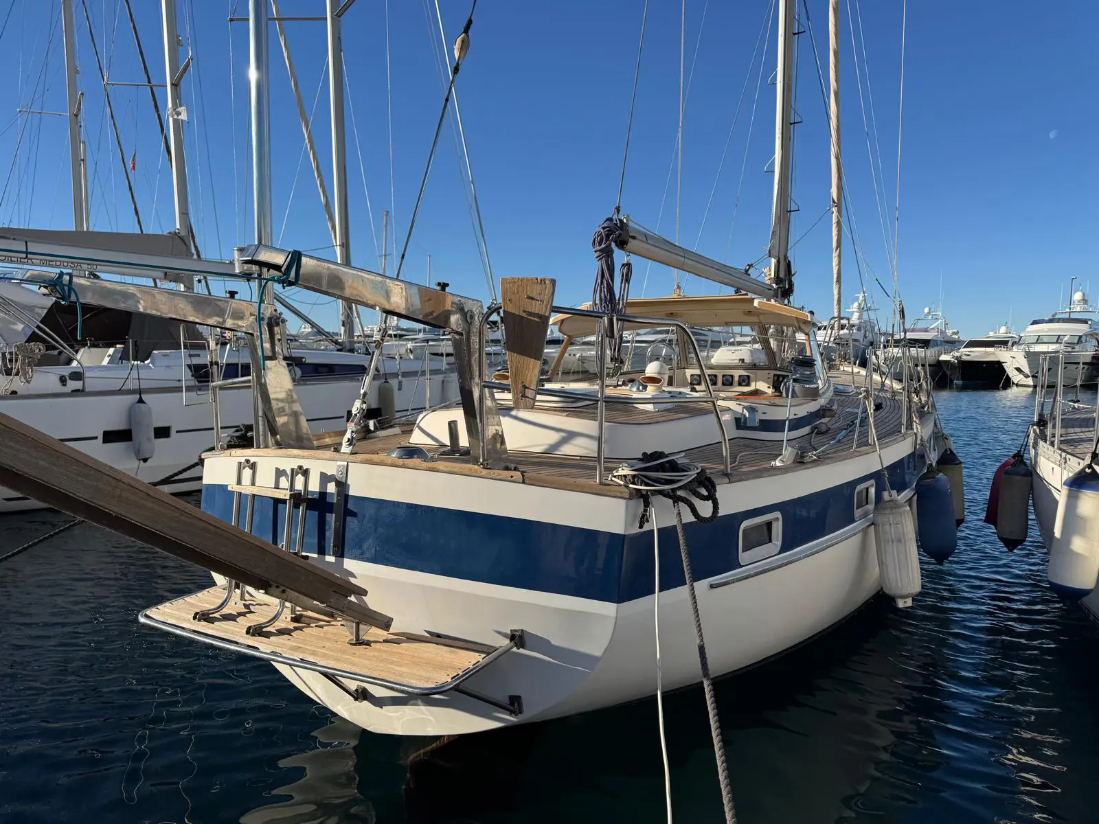 Hallberg Rassy 42 — Voilier bleu et blanc amarré dans un port, vu de trois quarts arrière.