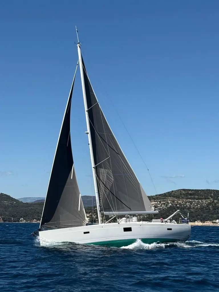 Hanse 455 — Voilier blanc à deux voiles noires naviguant près d'une côte vallonnée.