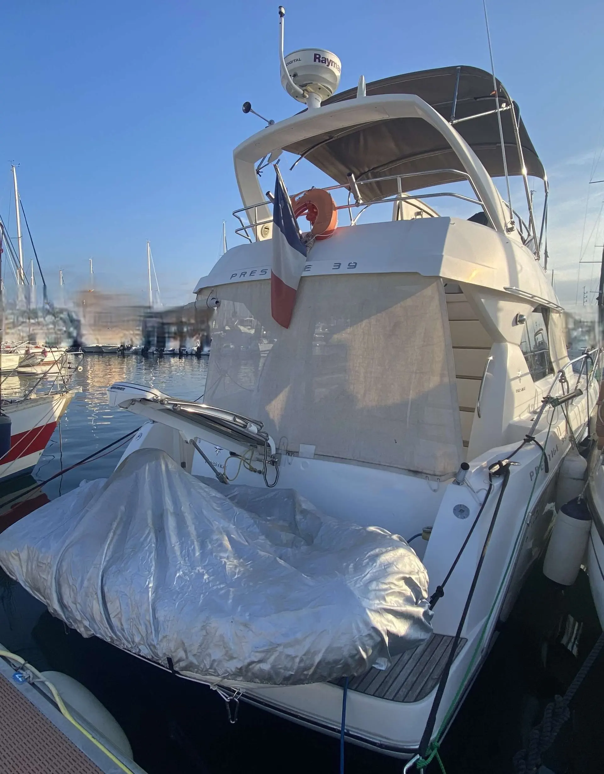 Jeanneau Prestige 39 — Bateau à moteur vu de l’arrière, amarré dans un port, avec annexe bâchée.