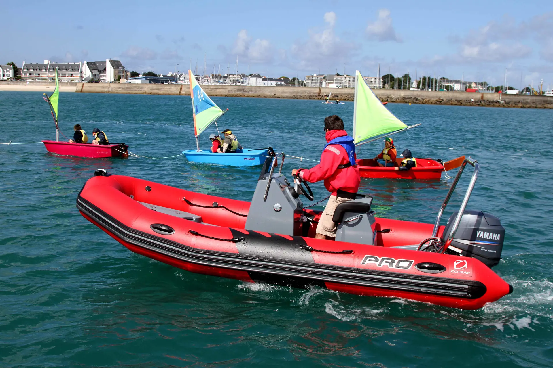 Zodiac Pro Classic 420 — Bateau pneumatique rouge à console évoluant sur l’eau, avec des voiliers en arrière-plan.
