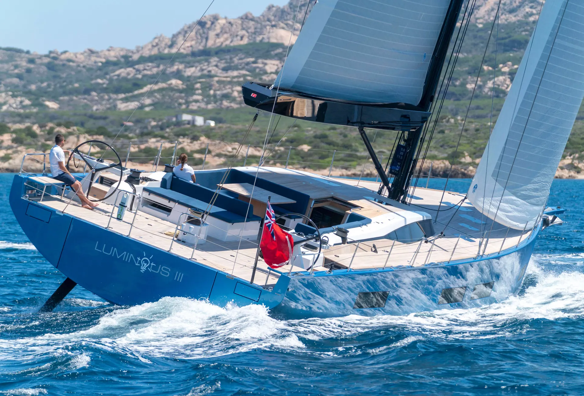Solaris 74 RS — Voilier bleu et blanc naviguant au près devant une côte rocheuse.