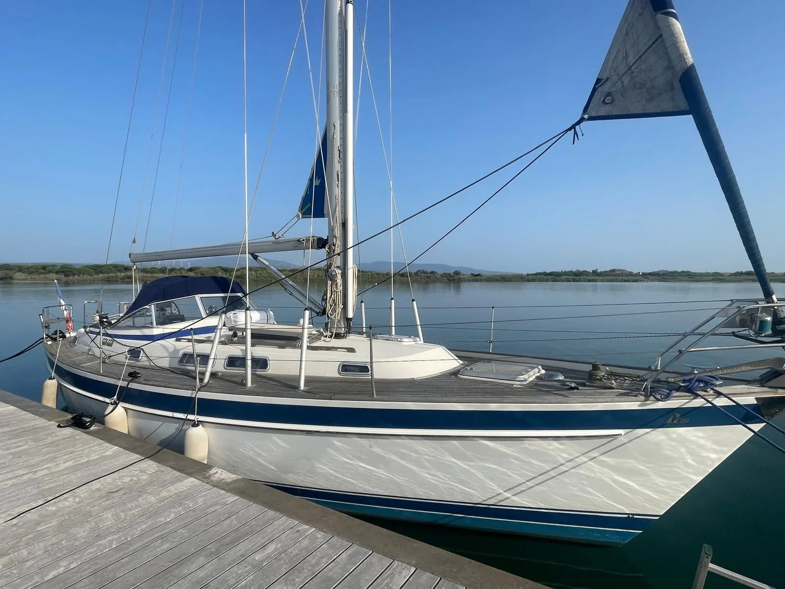 Hallberg Rassy 39 — Voilier amarré vu de profil depuis un ponton, sur une étendue d’eau calme.