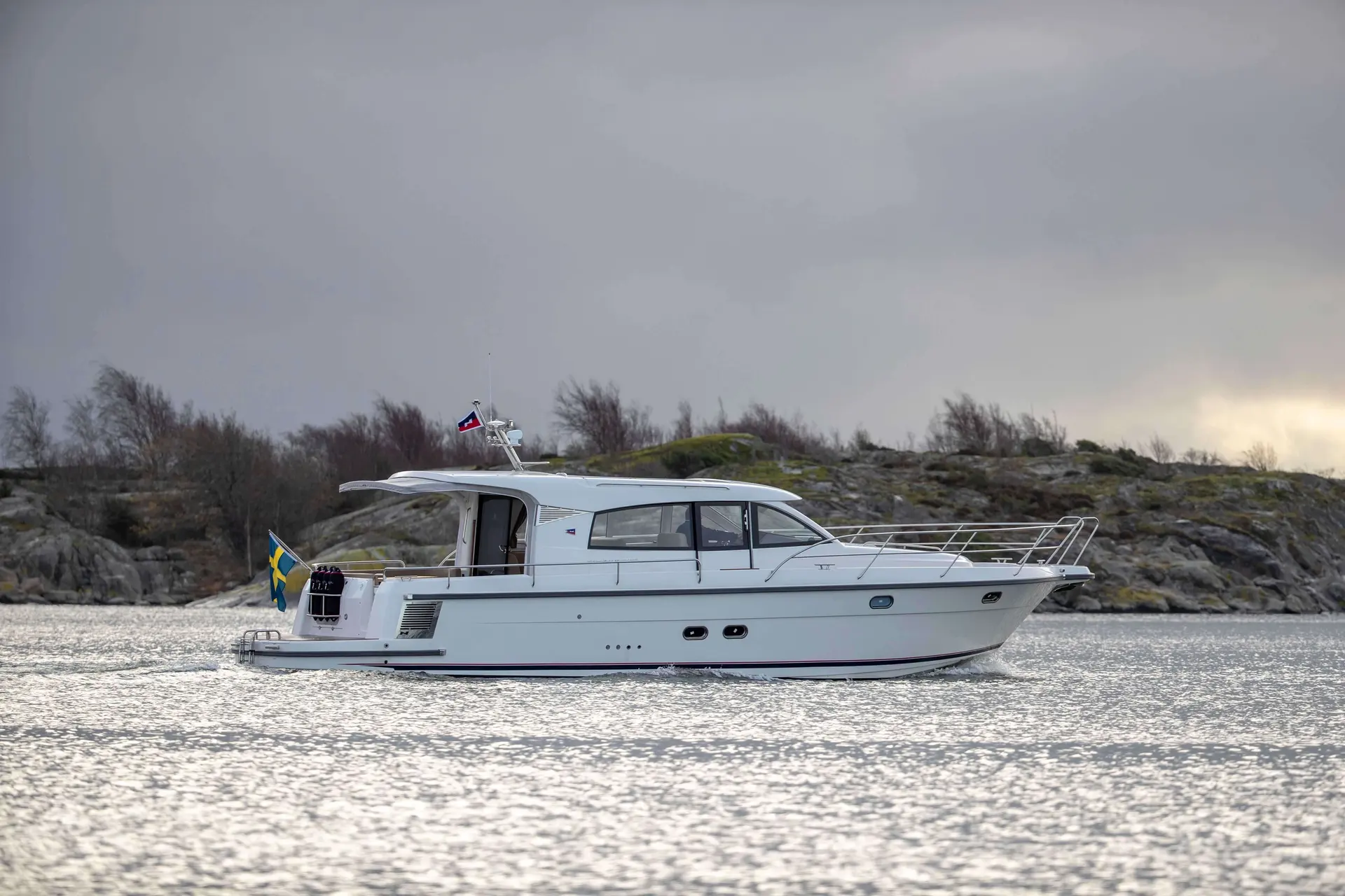 Nimbus 405 Coupe — Bateau à cabine blanc naviguant devant une côte rocheuse sous un ciel couvert.