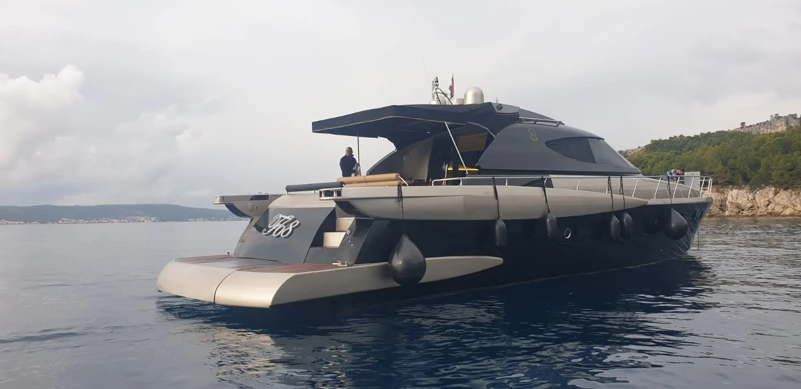 Fashion Yachts Fashion 68 — Yacht à moteur gris vu de trois quarts arrière, au mouillage près d’une côte.