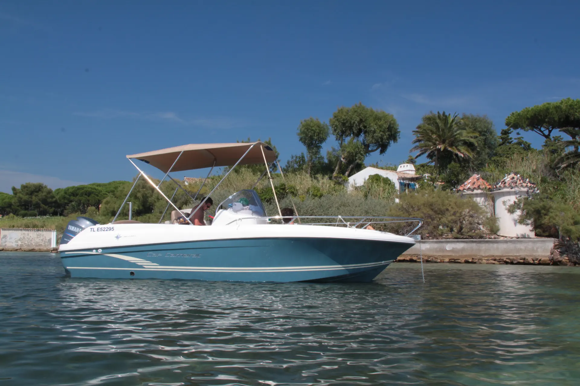 Jeanneau Cap Camarat 6.5 Style — Bateau à moteur vu de profil sur l’eau, avec taud de soleil et une personne à bord.
