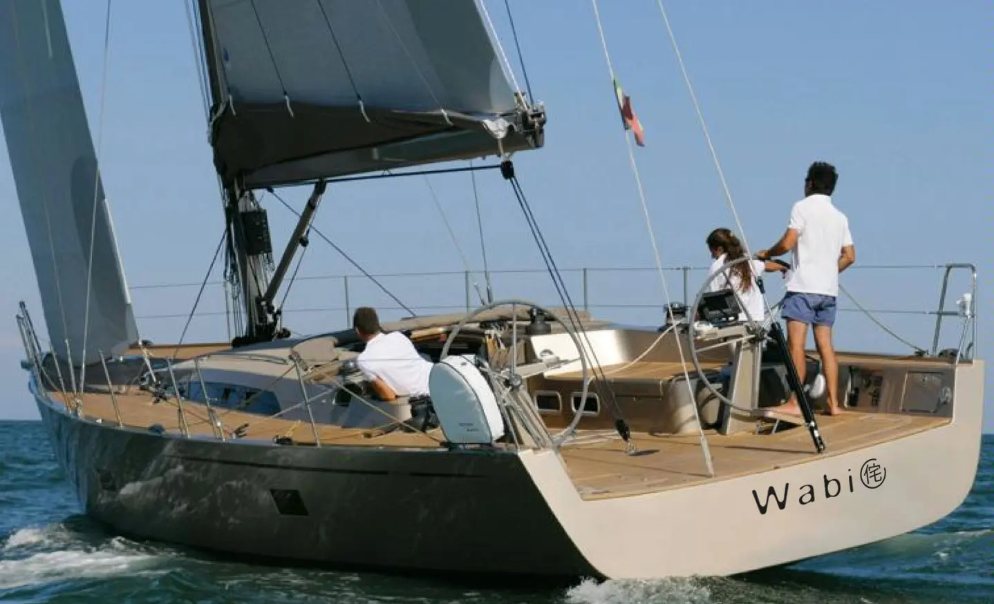 Sly Yachts 54 — Voilier vu de trois quarts arrière, en navigation, avec trois personnes à bord.