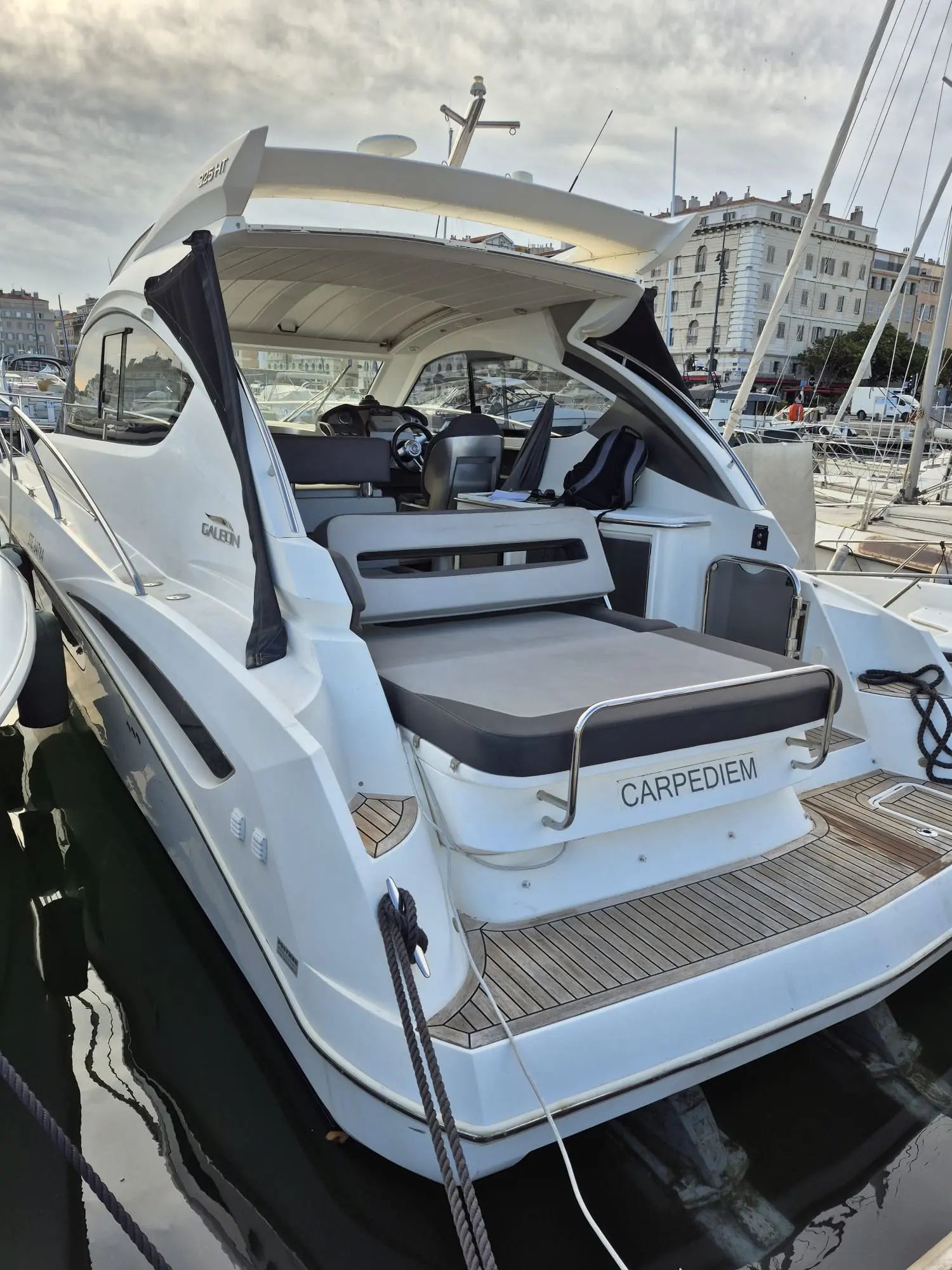 Galeon 325 HTO — Vue arrière d’un bateau à moteur dans un port, avec cockpit et plateforme de bain visibles.