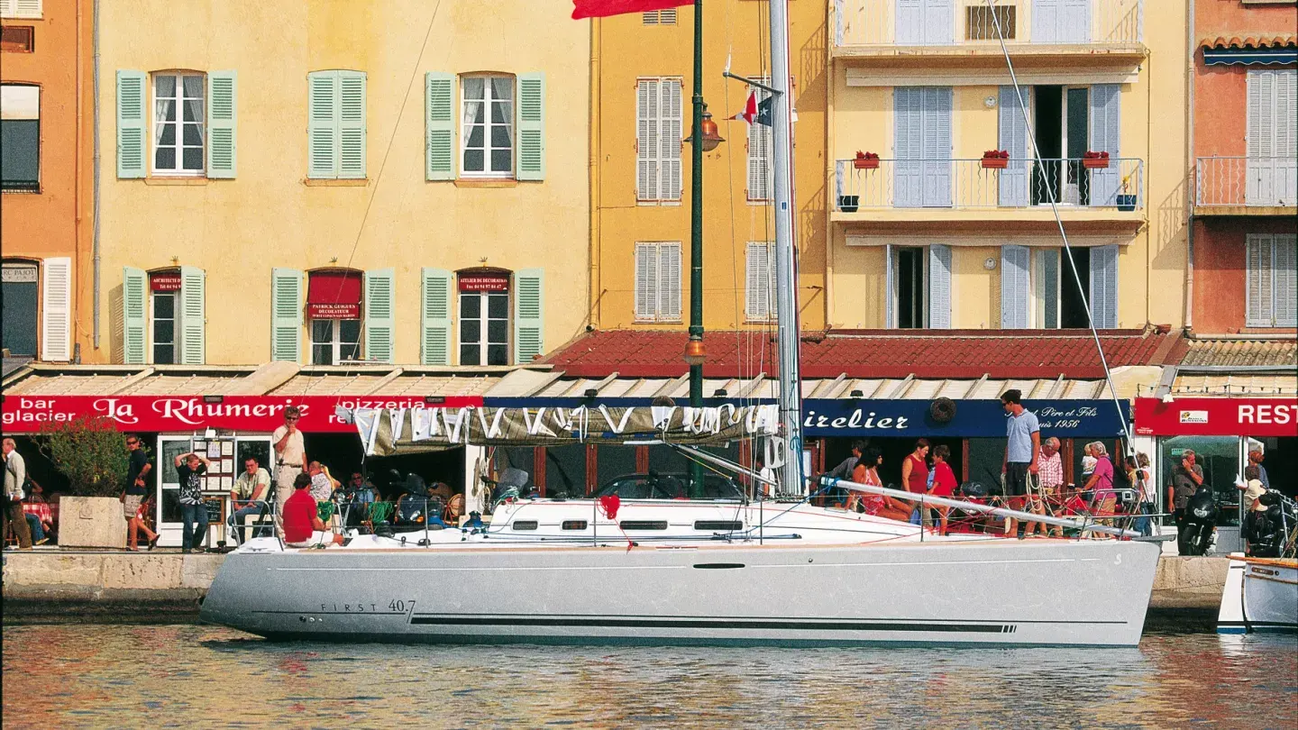 Beneteau First 40 — Voilier blanc vu de profil, amarré devant des commerces au bord de l’eau.