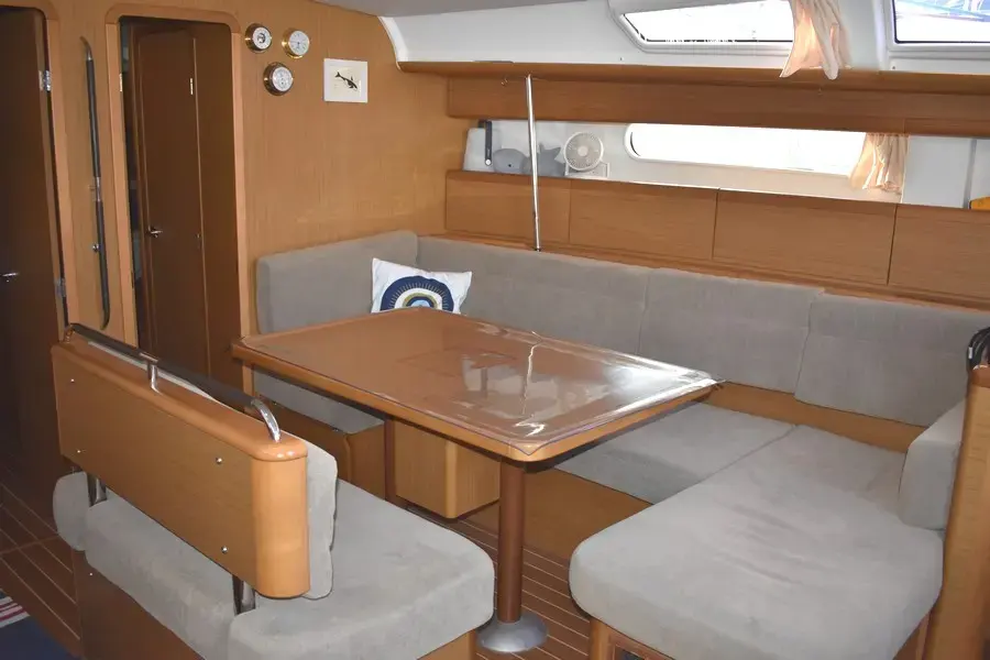 Jeanneau Sun Odyssey 49i — Vue du carré intérieur avec banquettes, table et rangements en bois.