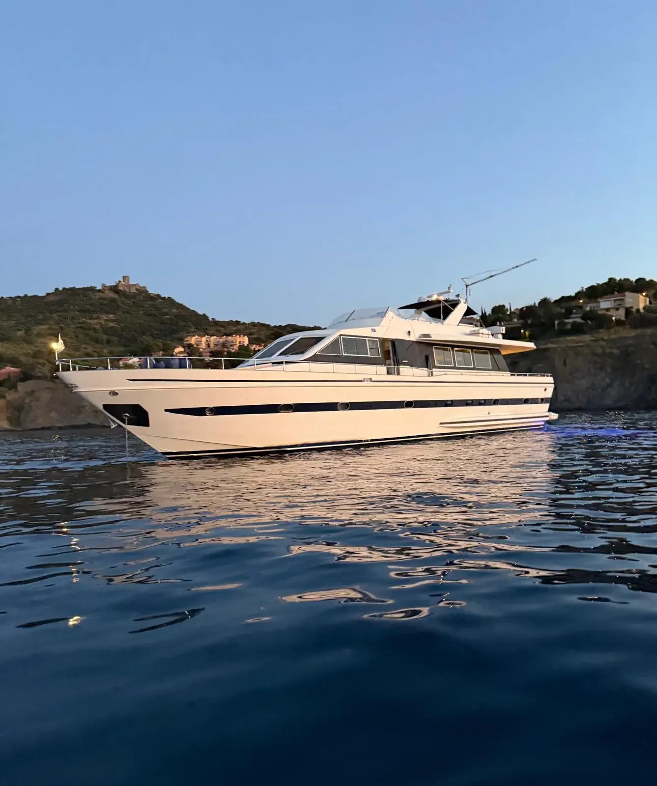 Falcon 80 — Vedette blanche vue de profil sur l’eau au crépuscule, devant une côte arborée.