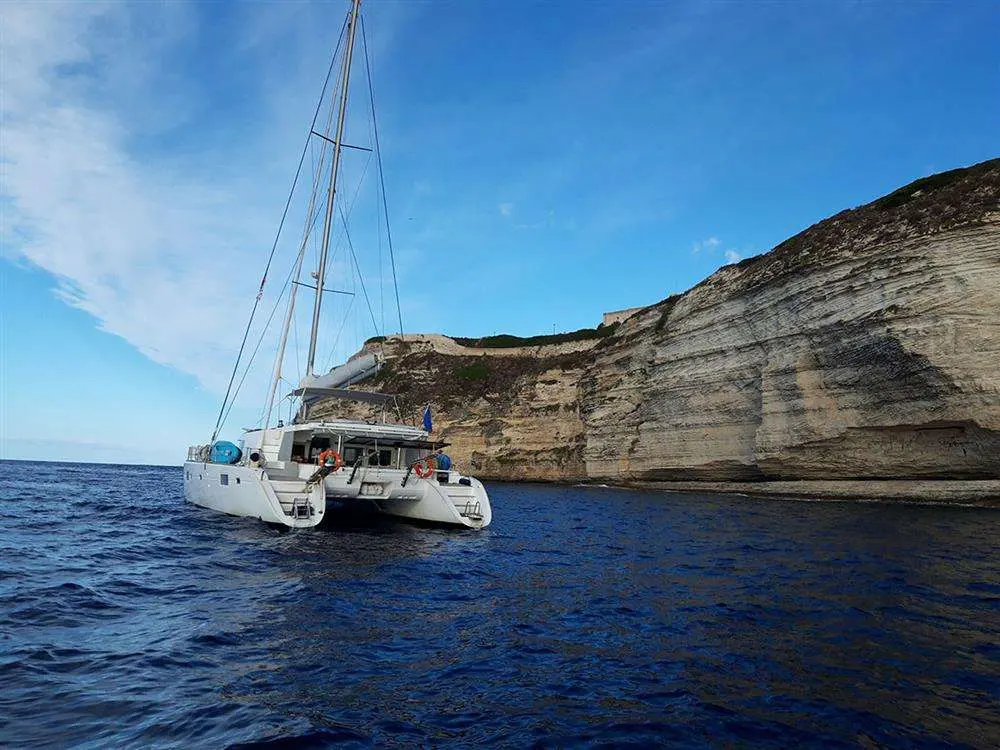 Lagoon 500 — Catamaran blanc photographié au mouillage devant une falaise stratifiée.