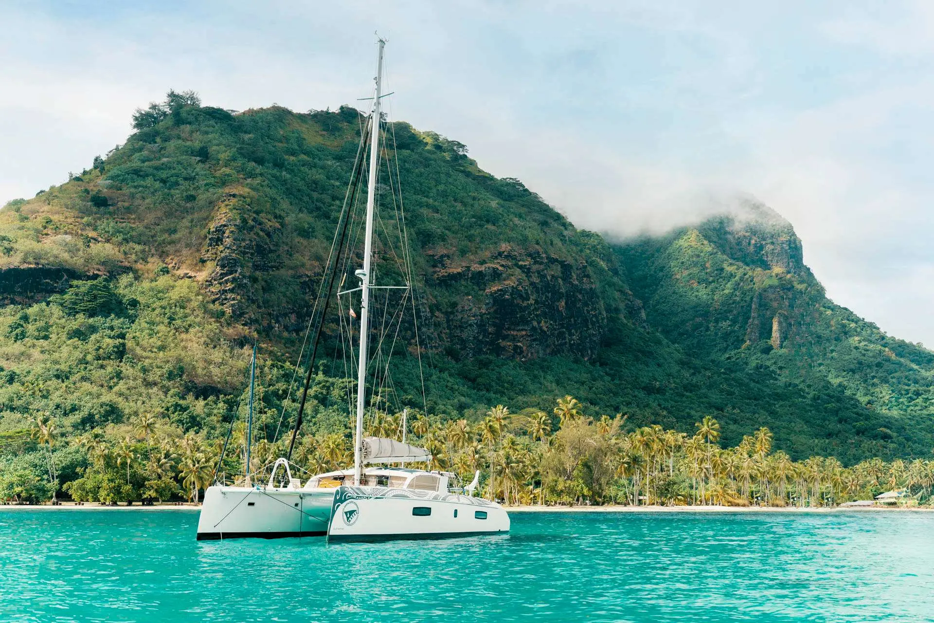 Outremer 51 — Catamaran blanc au mouillage devant une île tropicale montagneuse.