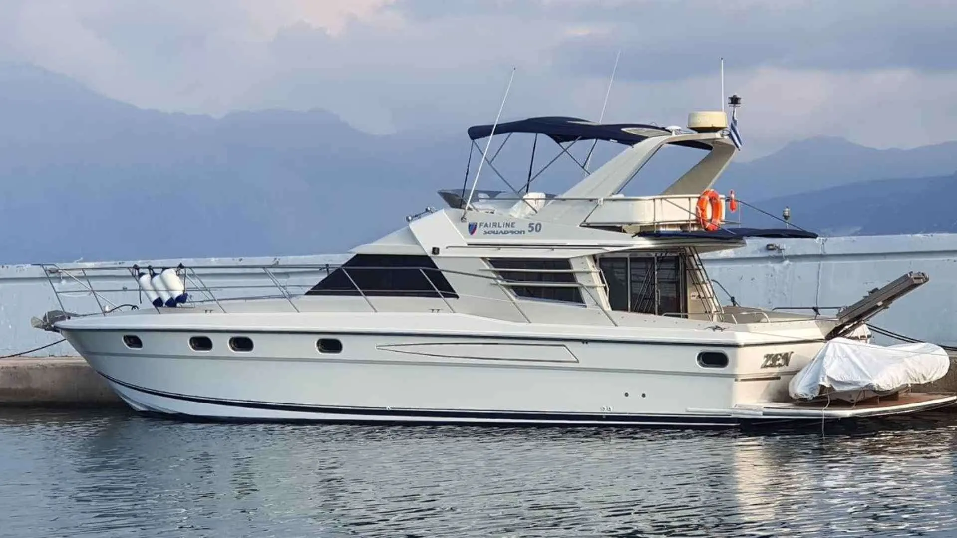 Fairline Squadron 50 — Vue latérale d’un bateau à moteur amarré dans un port, avec montagnes en arrière-plan.