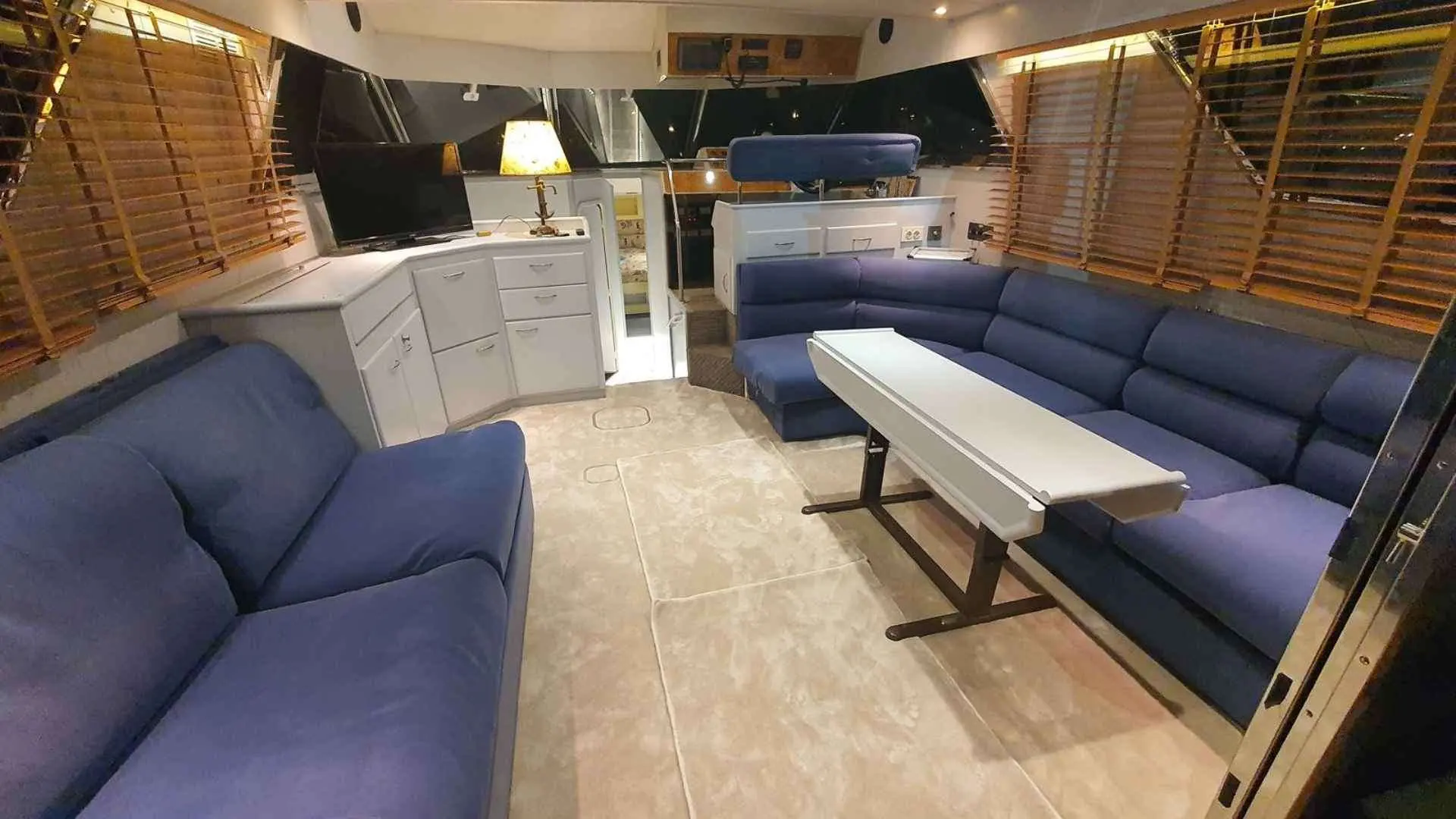 Fairline Squadron 50 — Salon intérieur avec banquettes bleues, table centrale et meuble de cuisine.