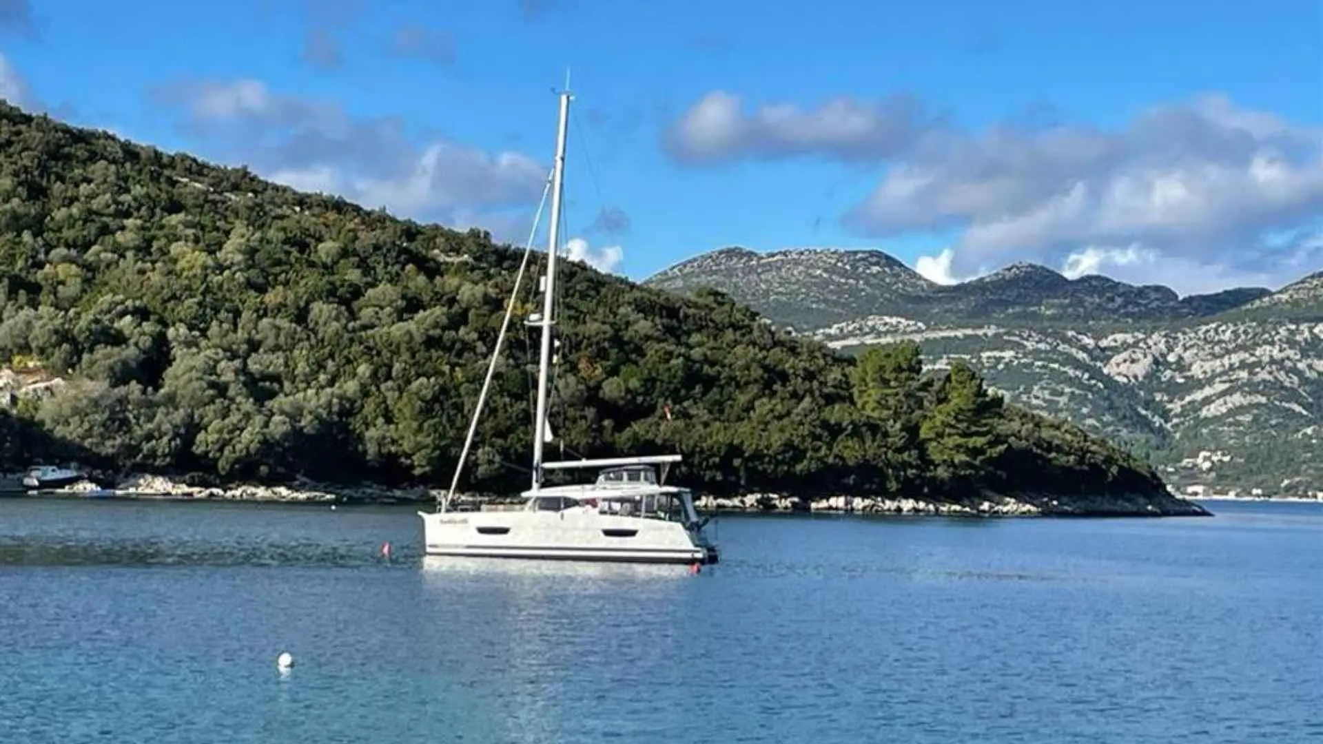 Fountaine Pajot Lucia 40 — Catamaran blanc au mouillage dans une baie entourée de reliefs boisés.