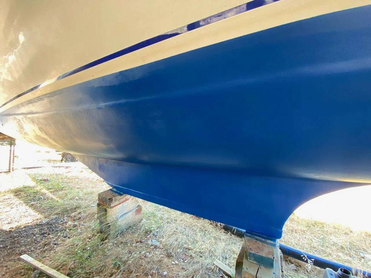 Custom Catamaran — Vue rapprochée de la coque bleue d’un bateau posé sur des supports à terre.