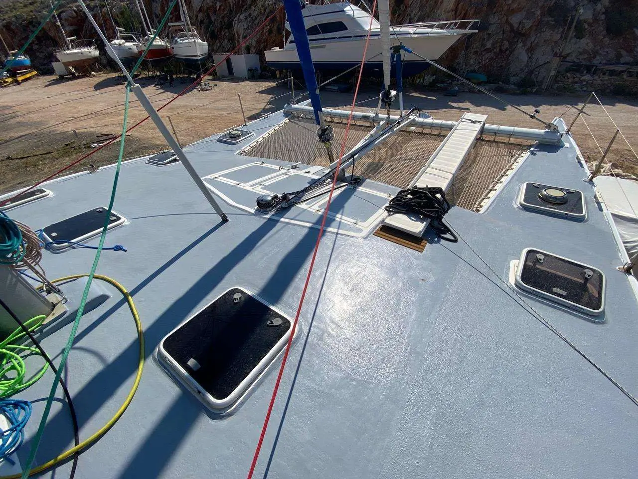 Custom Catamaran — Vue rapprochée du pont avant d’un catamaran à terre, avec trampolines et panneaux ouvrants.