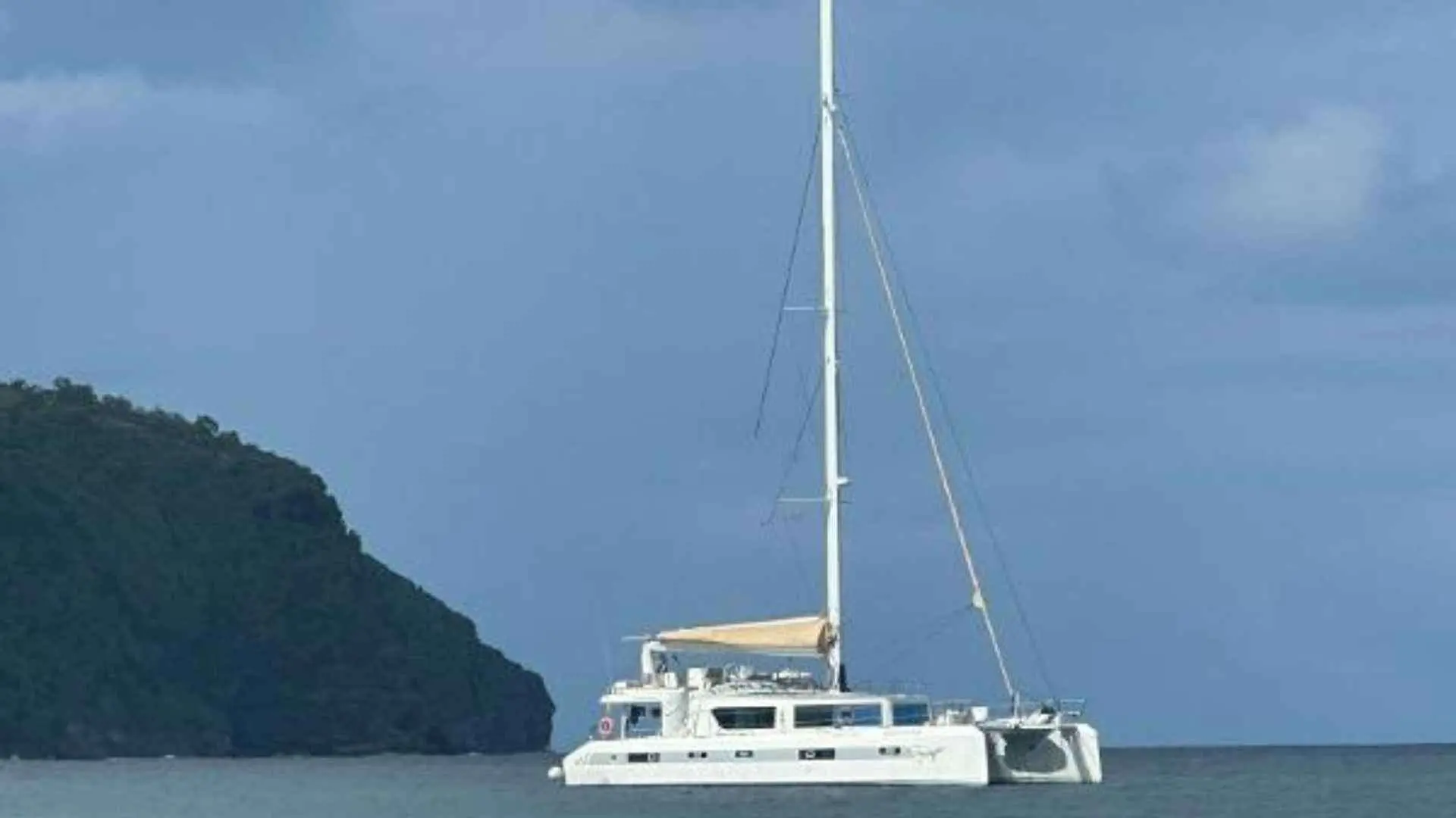 Squalt Marine International CK64 — Catamaran blanc au mouillage devant une île boisée, par temps nuageux.