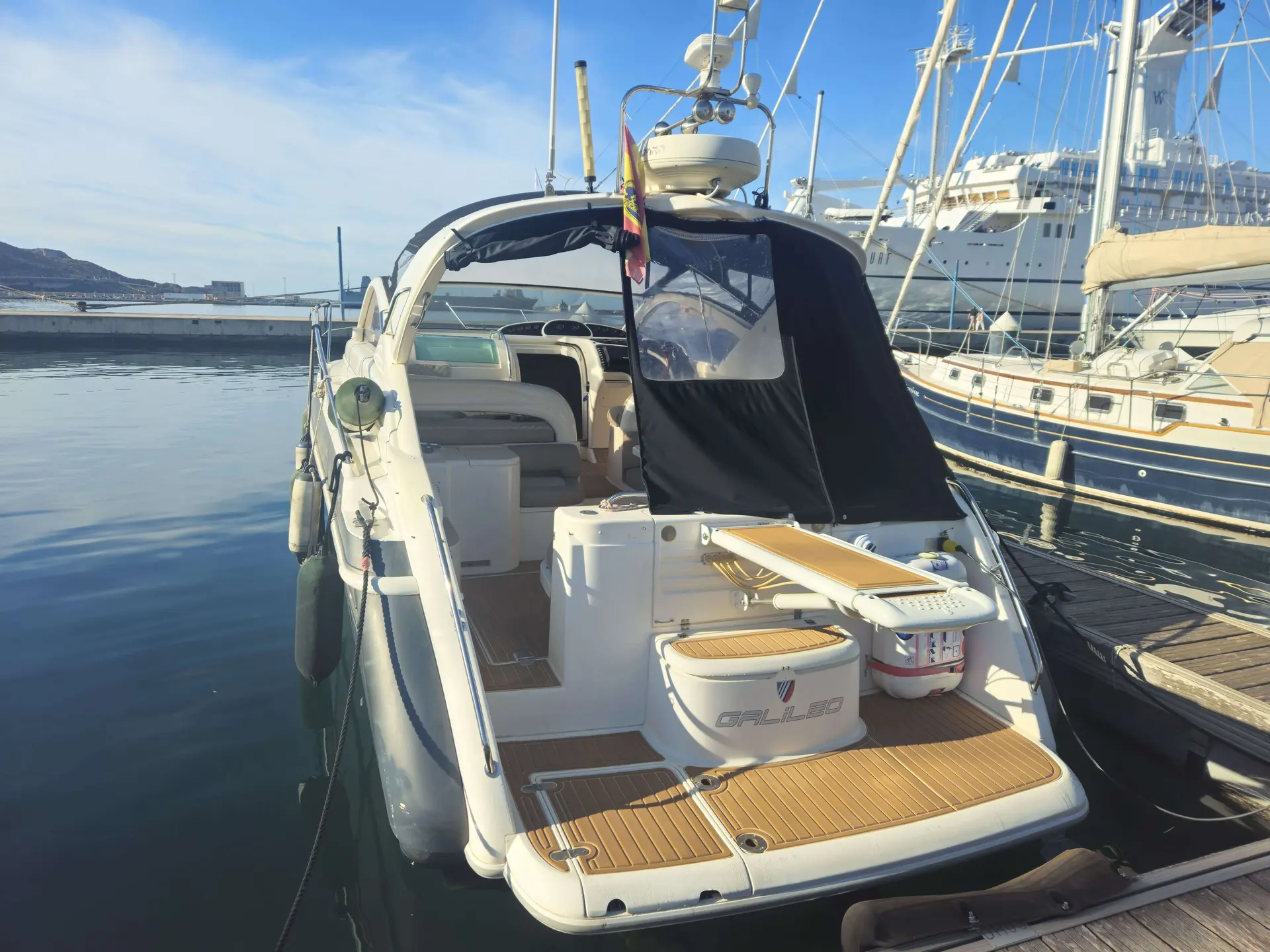 Fairline Targa 37 — Vue arrière d’un bateau amarré dans une marina, avec taud et plage de baignade.