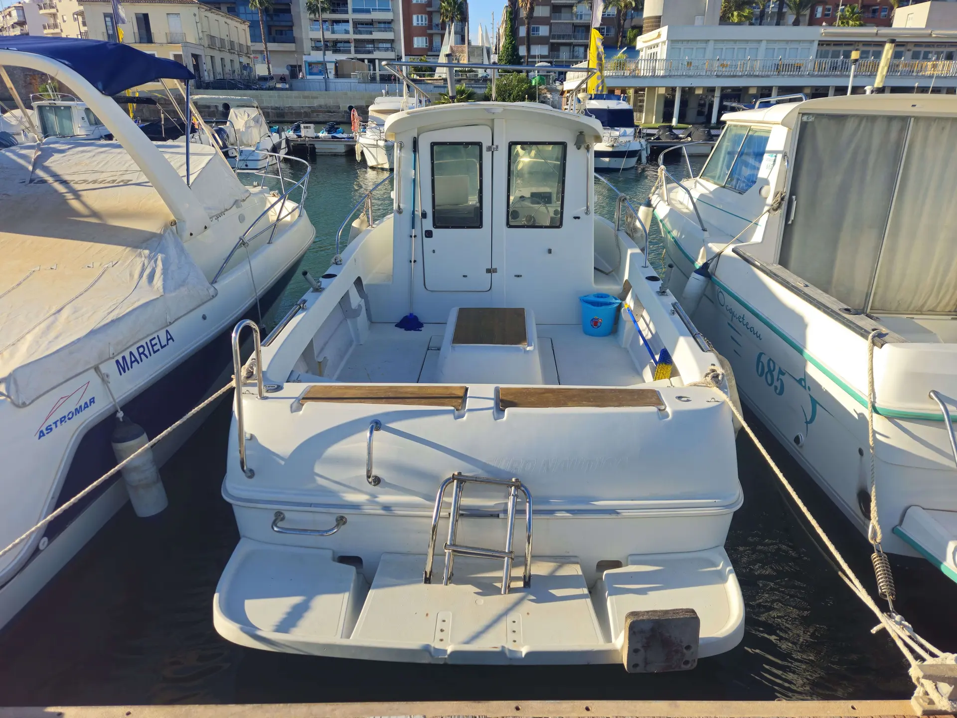 Arvor 20 — Vue arrière d’un bateau blanc amarré dans un port, entre deux autres embarcations.