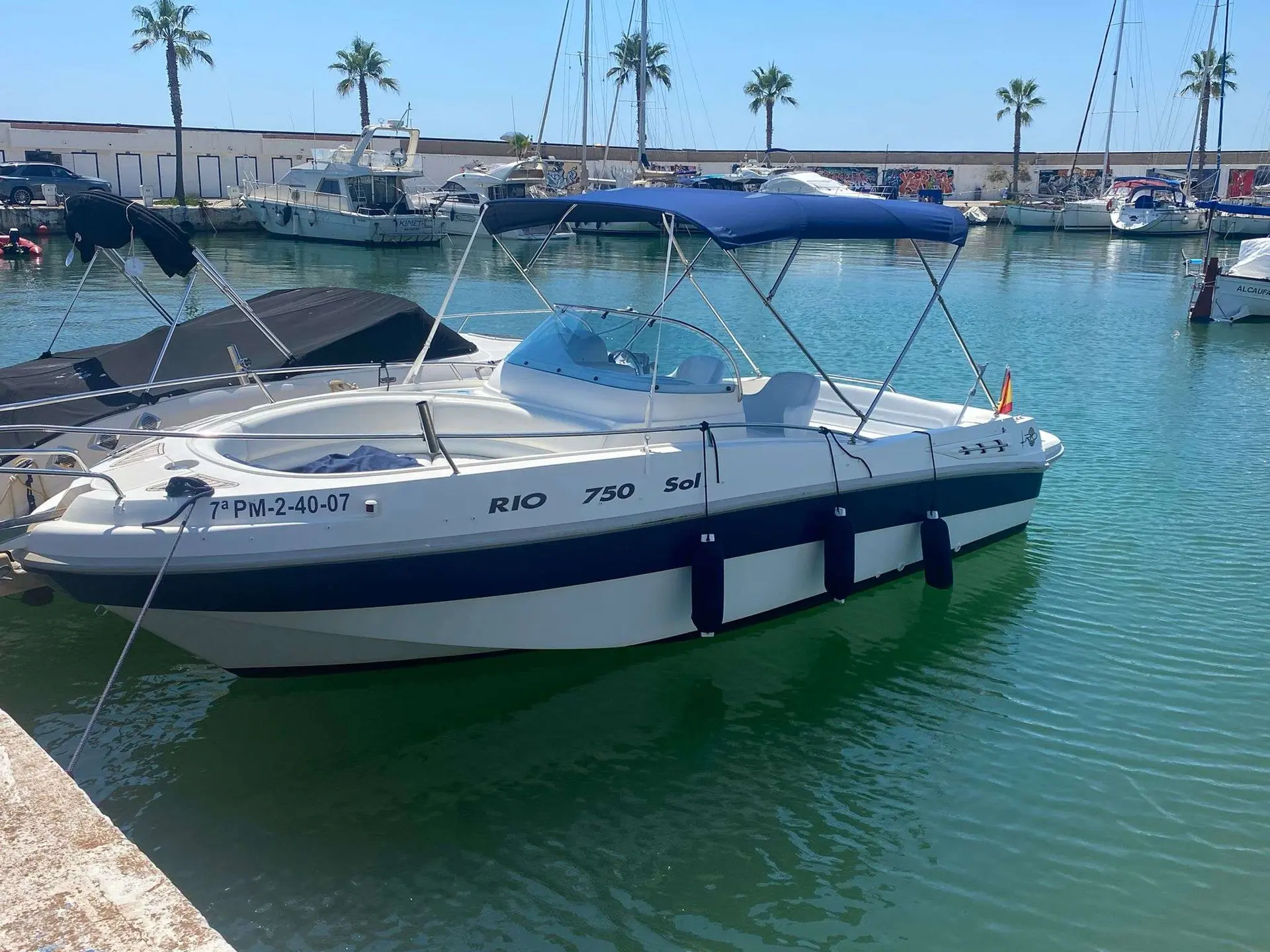 Rio 750 Sol — Bateau à moteur blanc et bleu amarré dans un port, vu de trois quarts bâbord.