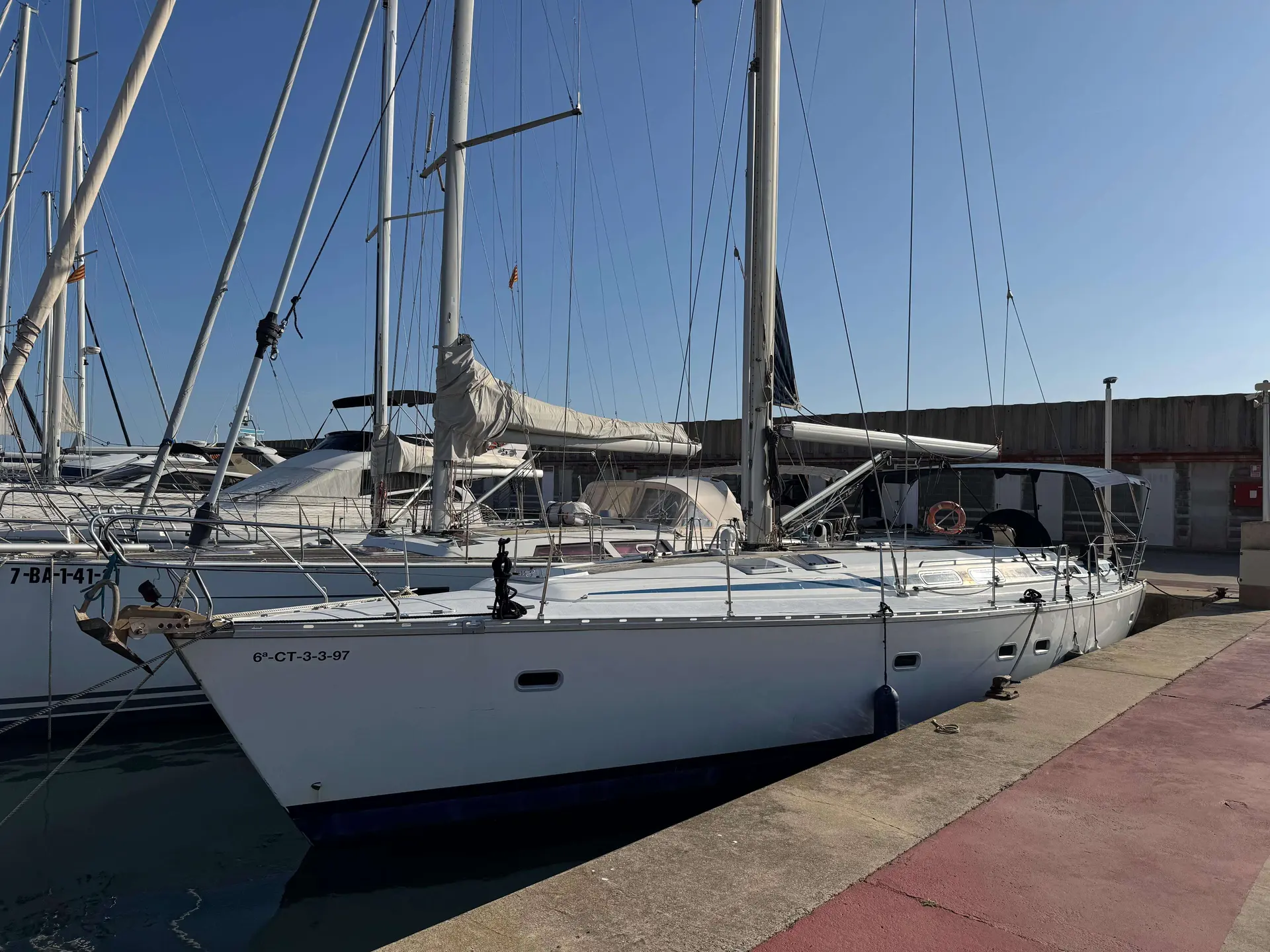 Bavaria 47 — Voilier blanc amarré au ponton, vu de trois quarts avec ses voiles affalées.