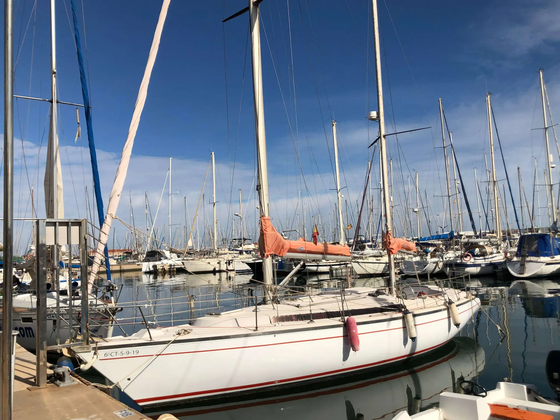 Jeanneau Gin Fizz — Voilier blanc à liserés rouges amarré dans un port, parmi de nombreux mâts.