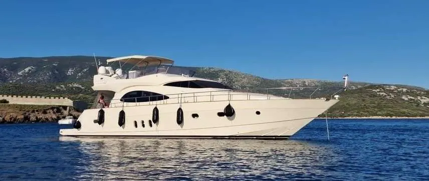 Cayman 62 Fly — Bateau à moteur vu de profil, amarré devant une côte rocheuse.
