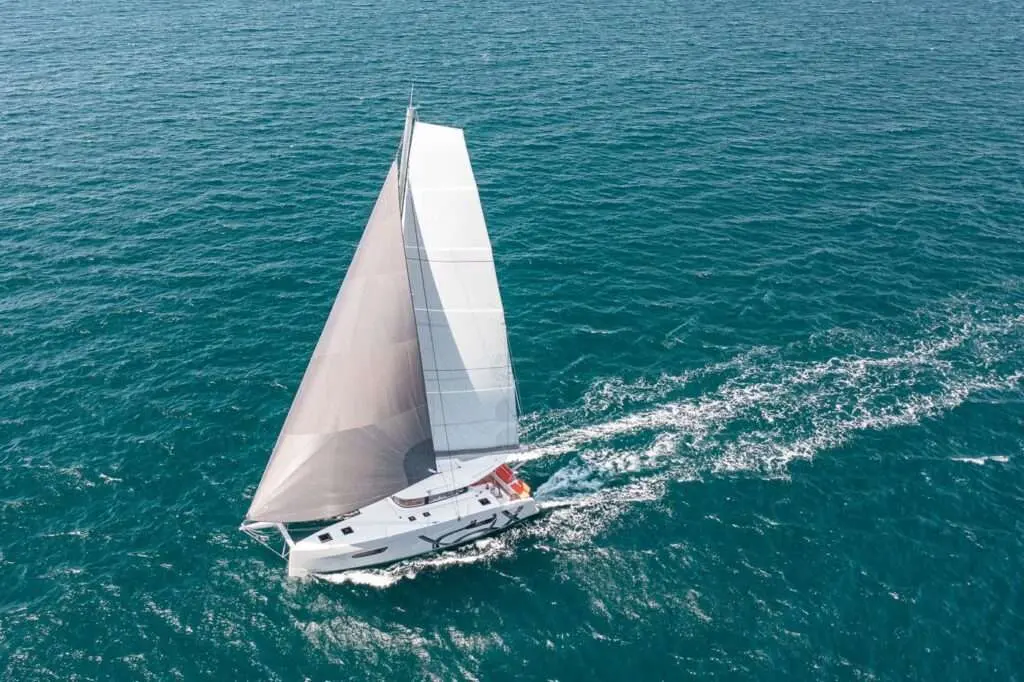 Excess Catamarans Excess 14 — Catamaran vu du ciel, toutes voiles déployées, naviguant sur une mer turquoise.