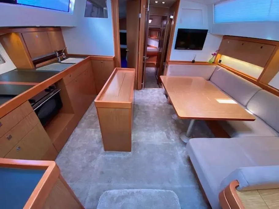 Beneteau Sense 43 — Vue intérieure du carré avec cuisine, banquette, table et téléviseur.