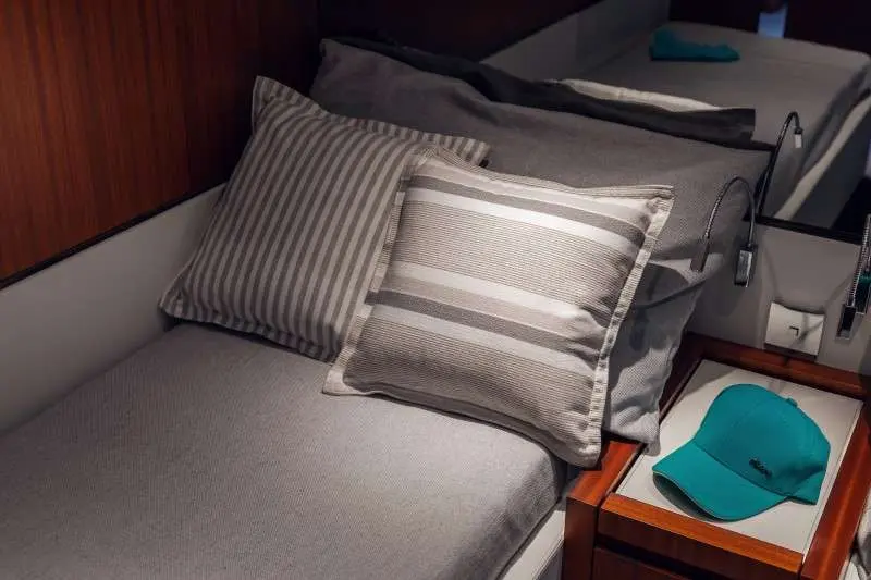 Riva 66 Ribelle — Couchette intérieure avec coussins et casquette turquoise.