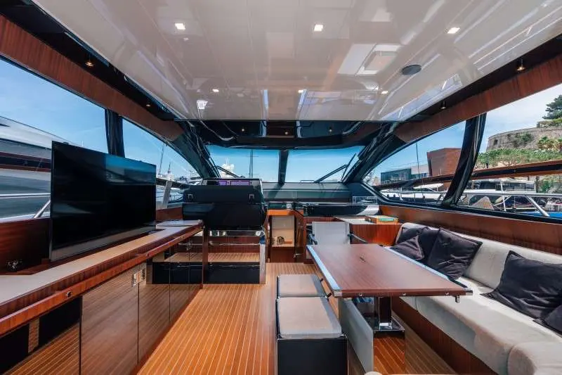 Riva 66 Ribelle — Vue intérieure du salon avec poste de pilotage, table et banquette.