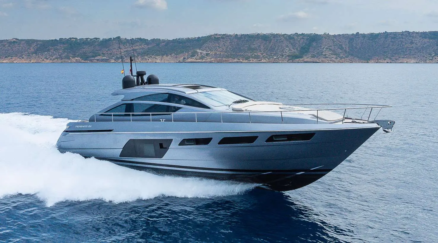 Pershing 6X — Yacht à moteur gris naviguant rapidement devant une côte escarpée.
