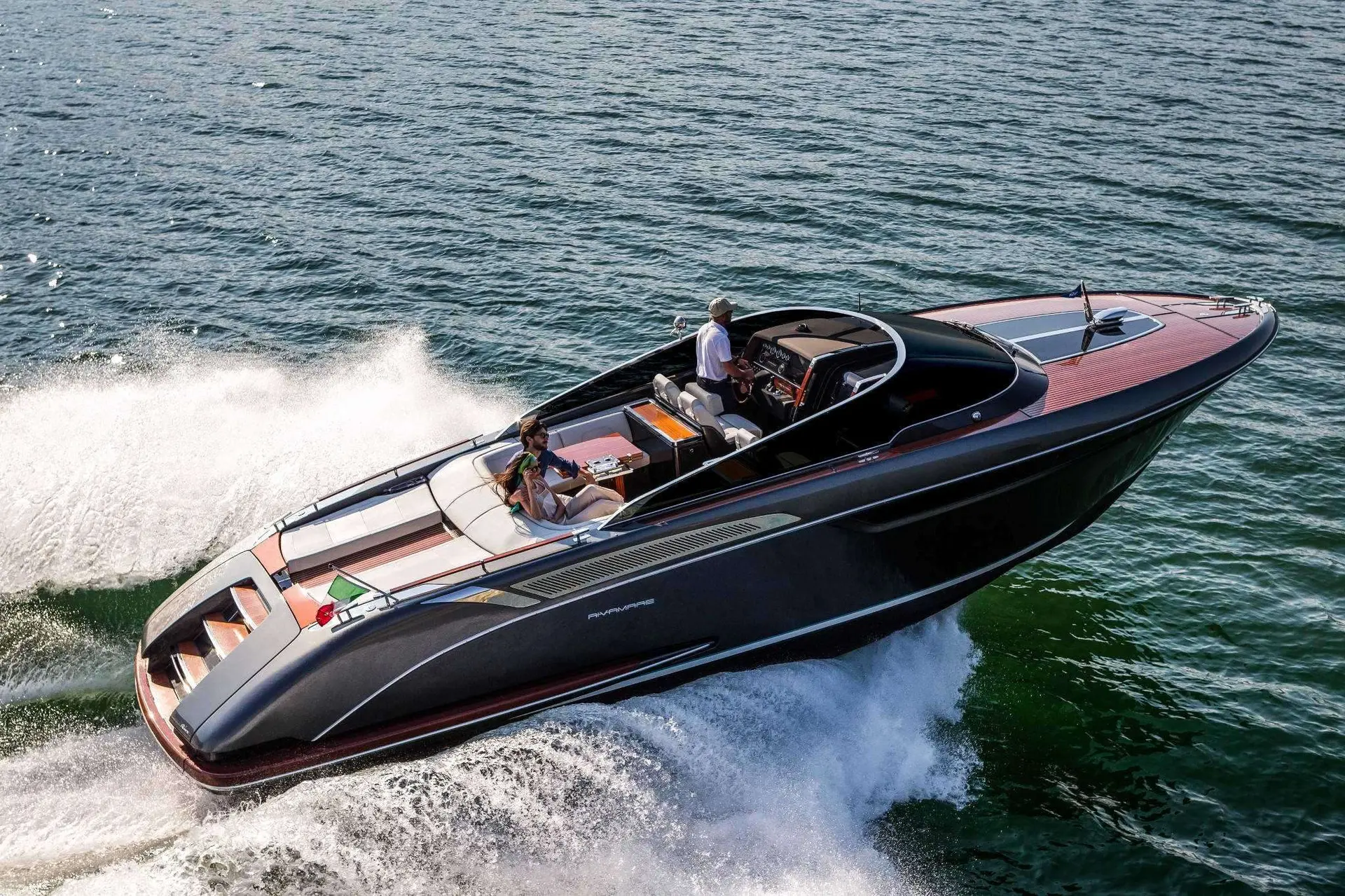 Riva 38 Bravo — Bateau à moteur noir et acajou naviguant rapidement, vu en trois-quarts depuis les airs.