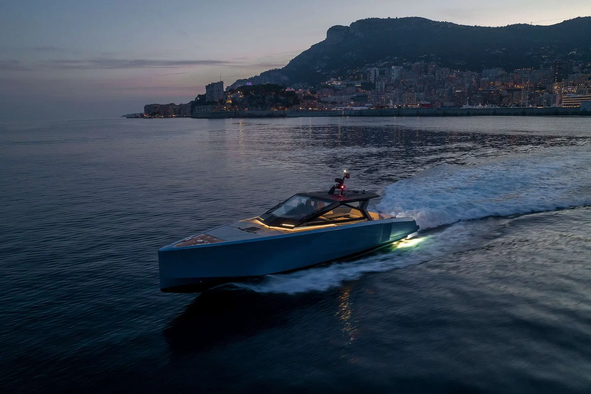 Wally Power 58 — Bateau à moteur bleu naviguant au crépuscule devant une ville côtière.