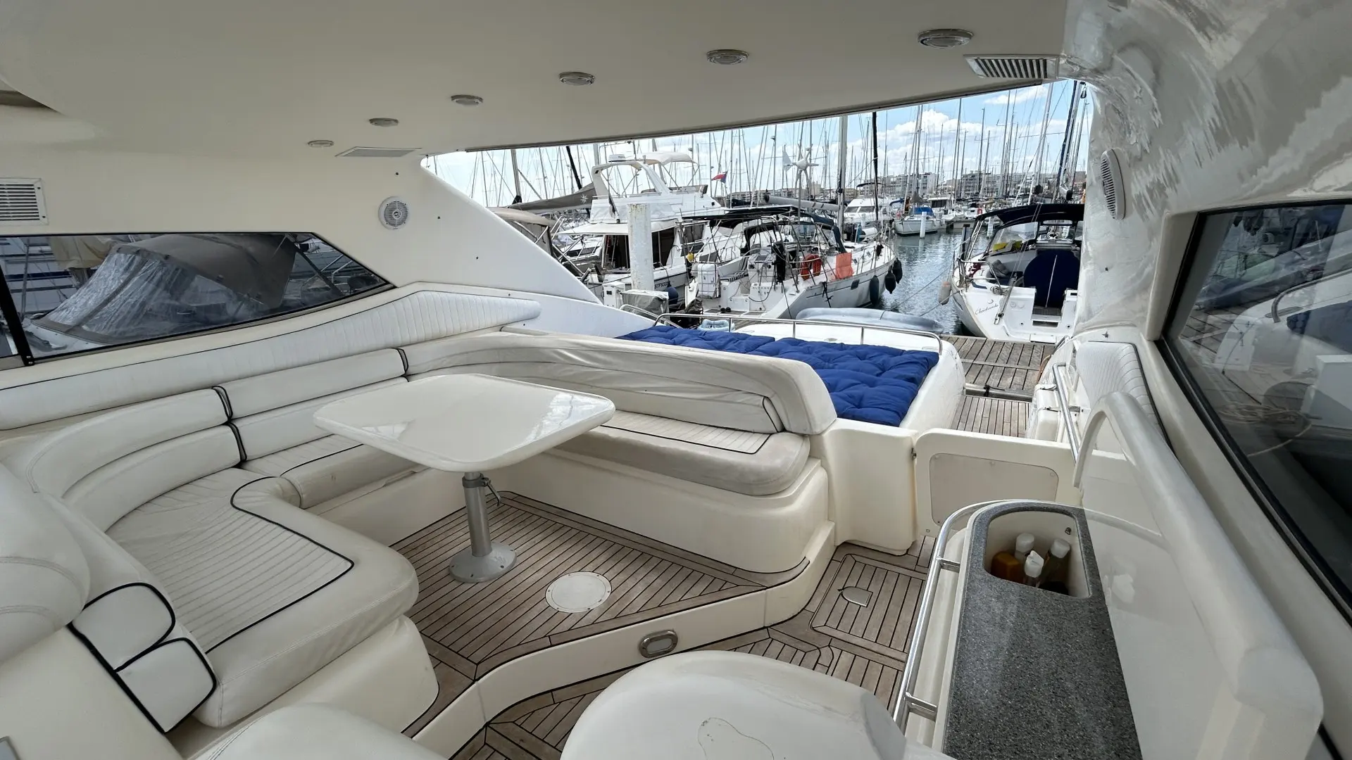 Sunseeker Predator 63 — Cockpit arrière avec banquette en U, table et bain de soleil dans un port.
