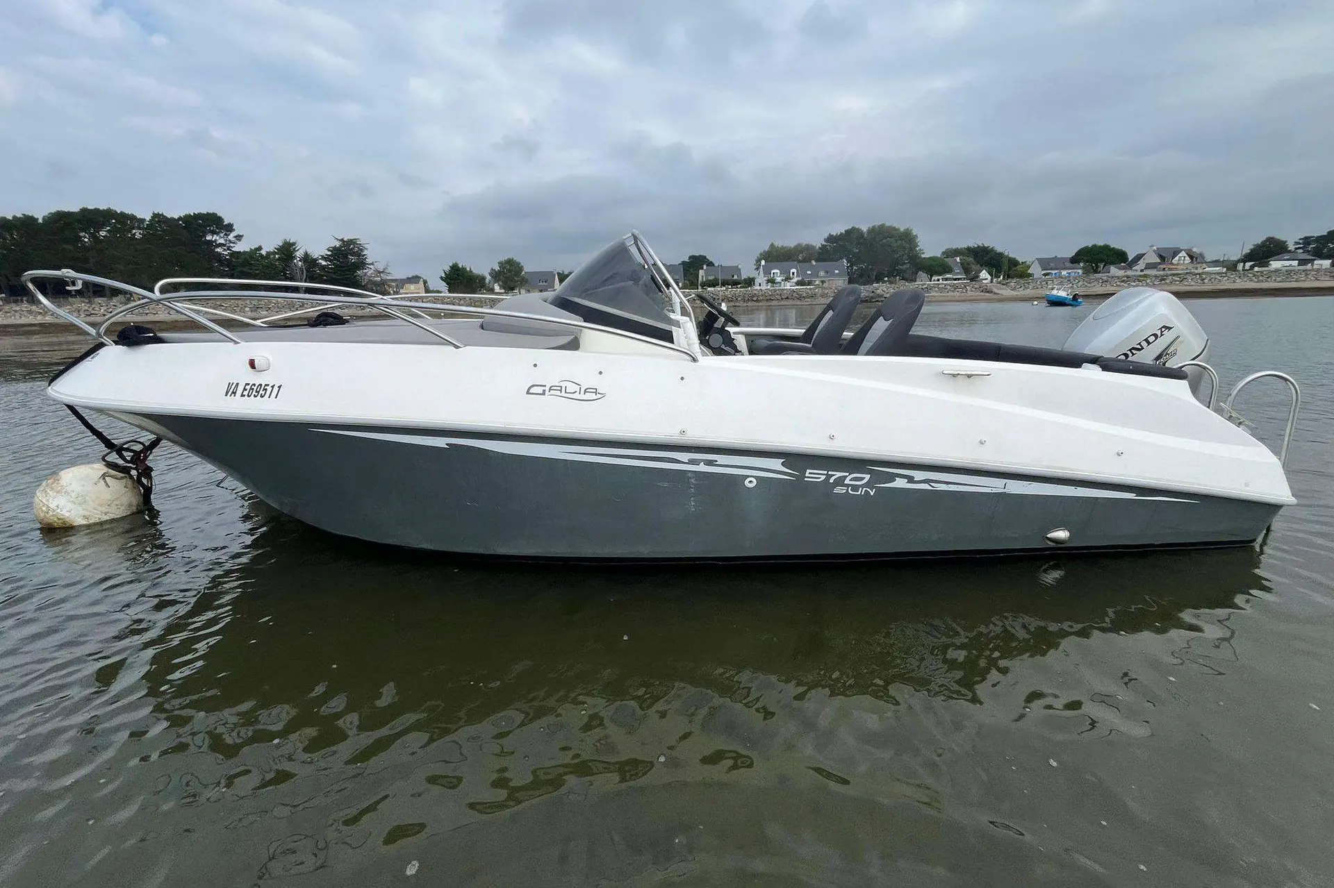 Galia 570 Sun Deck — Bateau à moteur blanc photographié de profil sur l’eau, avec console centrale et hors-bord.