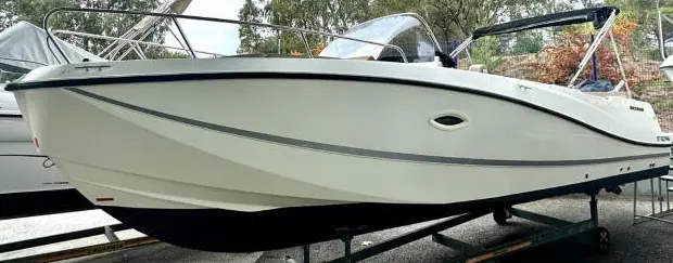Quicksilver 750 Week-End — Bateau à moteur blanc présenté sur remorque, vu de profil dans un espace extérieur.