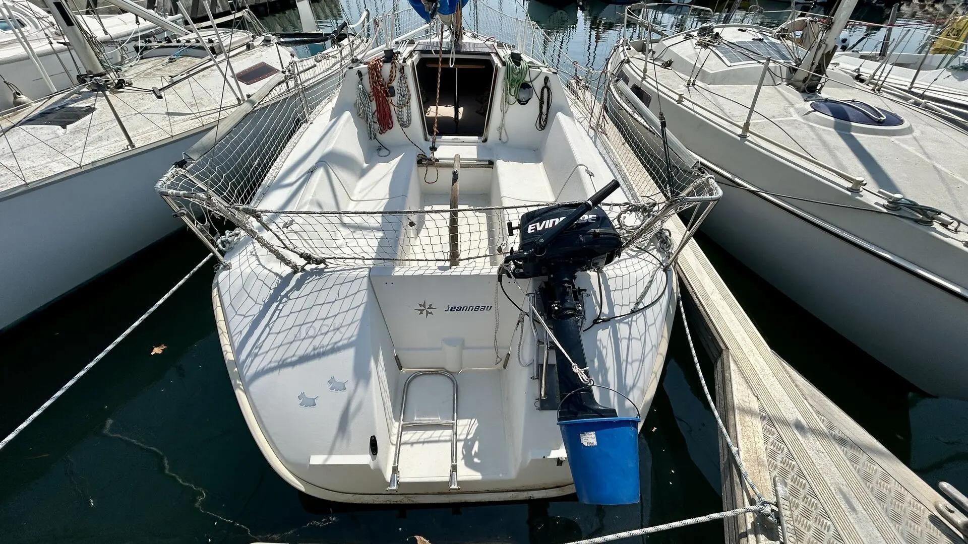 Jeanneau Sun Way 21 — Voilier blanc vu de l’arrière, amarré entre deux bateaux, avec moteur hors-bord.