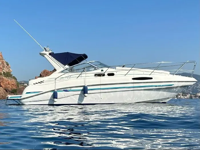 Sealine Bolero 28 — Bateau à moteur blanc photographié de profil sur l’eau, près d’une côte rocheuse.